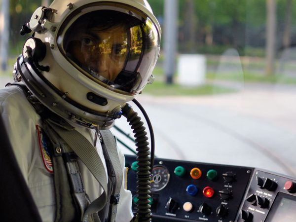 Ein Astronaut sitzt am Fahrerarbeitsplatz einer Straßenbahn und blickt nach hinten.