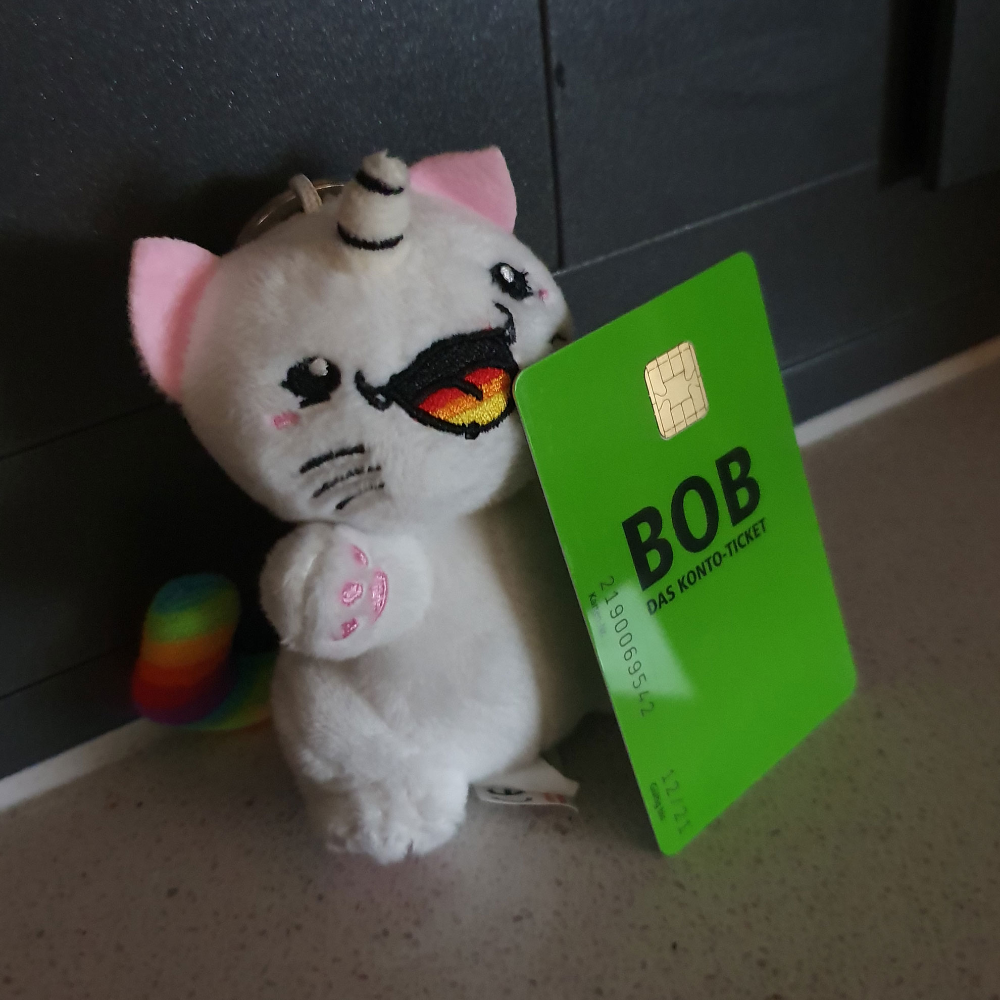 Ein kleines weißes Stofftier-Einhorn hält eine grüne Plastik-Karte im EC-Karten-Format vor sich: Das BOB-Konto-Ticket der BSAG.