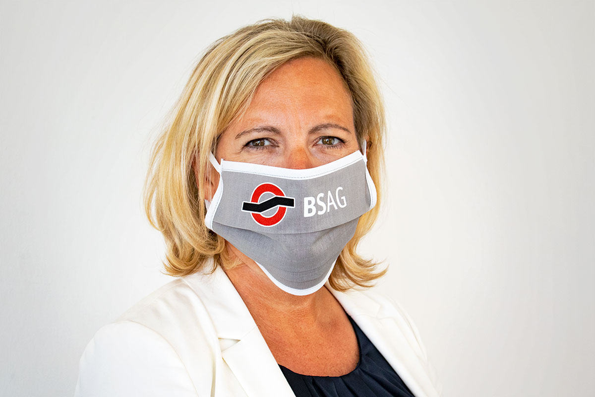 Eine Frau mit einer grauen Mund-Nasen-Bedeckung mit BSAG-Logo.