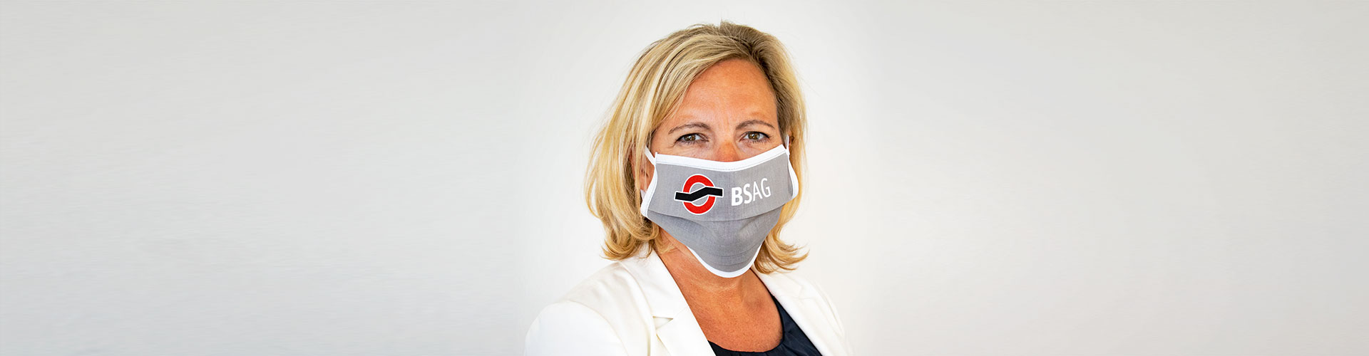 Eine Frau mit einer grauen Mund-Nasen-Bedeckung mit BSAG-Logo.