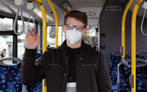 Ein junger Mann steht im Bus und trägt eine FFP2-Maske.